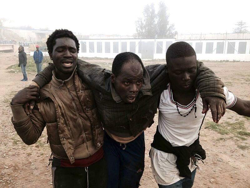 Uno de los inmigrantes herido es auxiliado por dos de sus compañeros tras el asalto a la valla en Melilla. / Fernando Gutierrez (Efe)