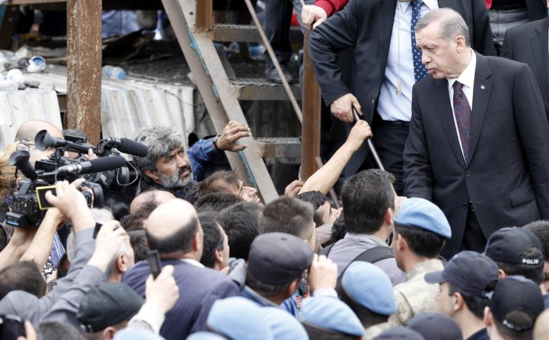 El primer ministro turco, Tayyip Erdogan, en la parte superior derecha, ha sido increpado por los familiares y compañeros de los mineros cuando ha visitado la zona. / Tolga Bozoglu (Efe)