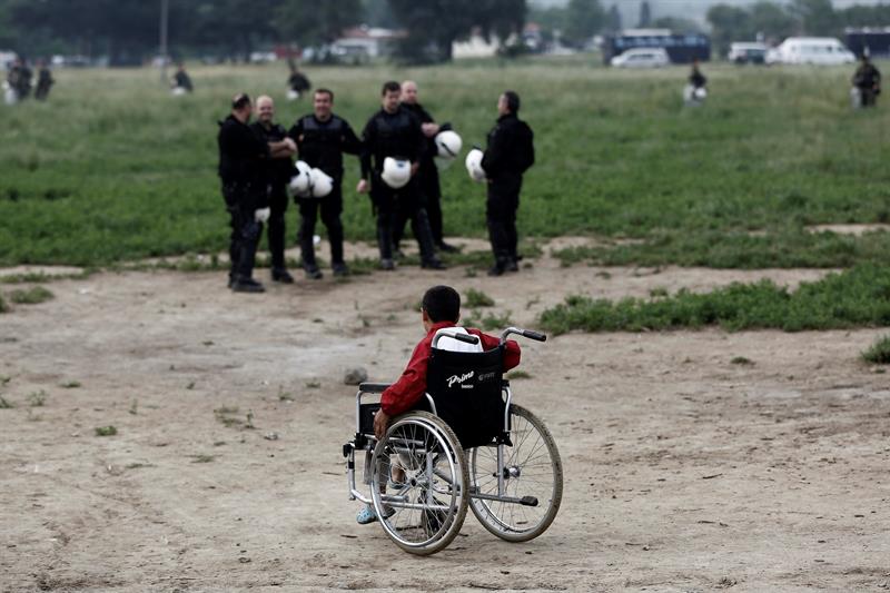 Un niño refugiado en silla de ruedas pasa junto a un grupo de policías durante el desalojo del campamento.
