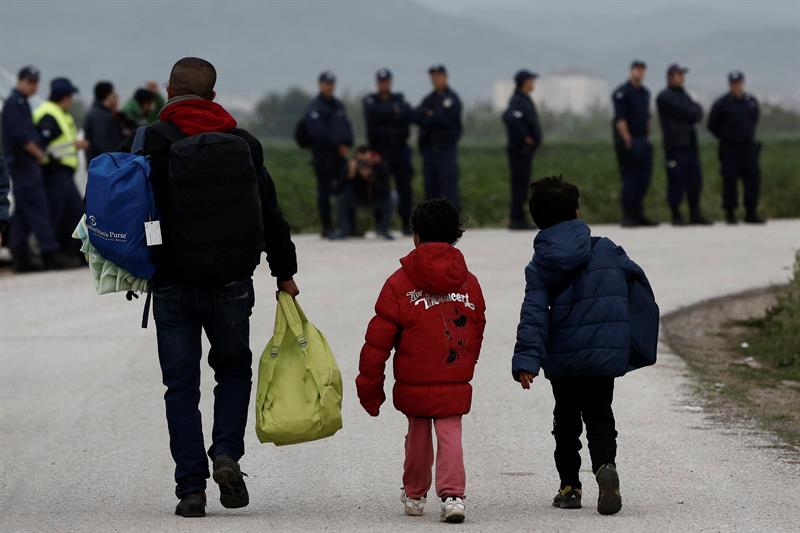 Un refugiado adulto y dos niños, con sus pertenencias, esta mañana, durante el operación que ha iniciado la policía griega para desalojar del campamento improvisado de Idomeni, en la frontera con Macedonia. / Reportaje fotográfico de Yannis Kolesidis (Efe)