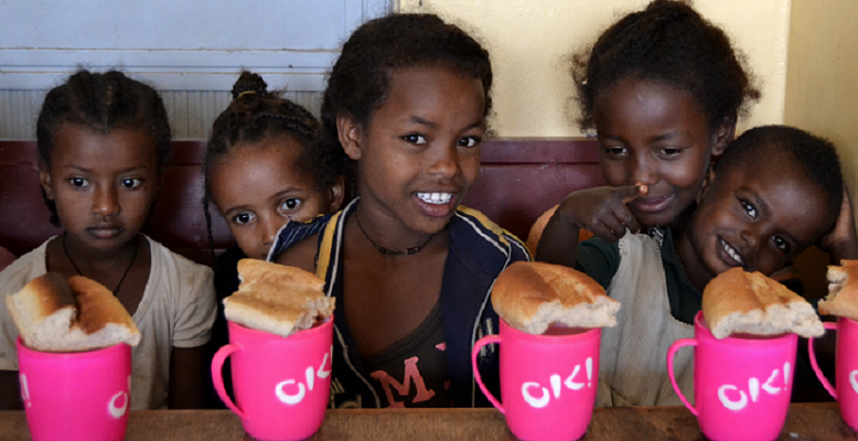 Share a Coffee For Niñas de la guardería de Debre Zeit, en Etiopía, sonríen frente a sus tazones de desayuno, subvencionados gracias a los cafés solidarios