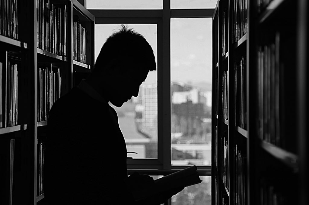 Silueta de un hombre, en una imagen tomada en contraluz, leyendo en una biblioteca.