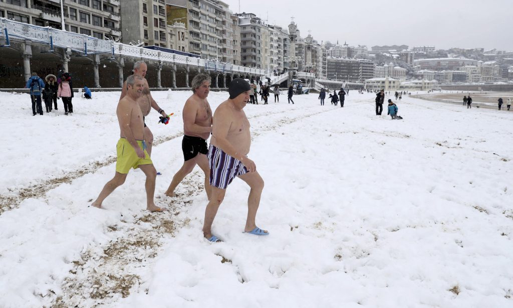 Un grupo de bañistas se dirigen al agua en la playa de La Concha de San Sebastián, cubierta de nieve