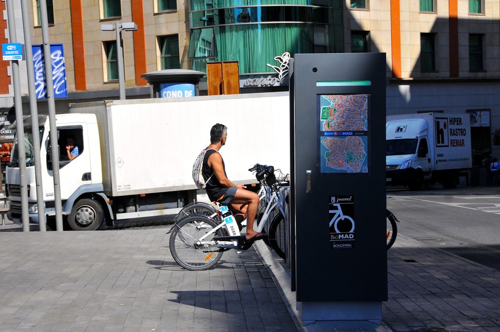 Un hombre permanece montado en una bicicleta de BiciMAD, anclada en su poste de estacionamiento