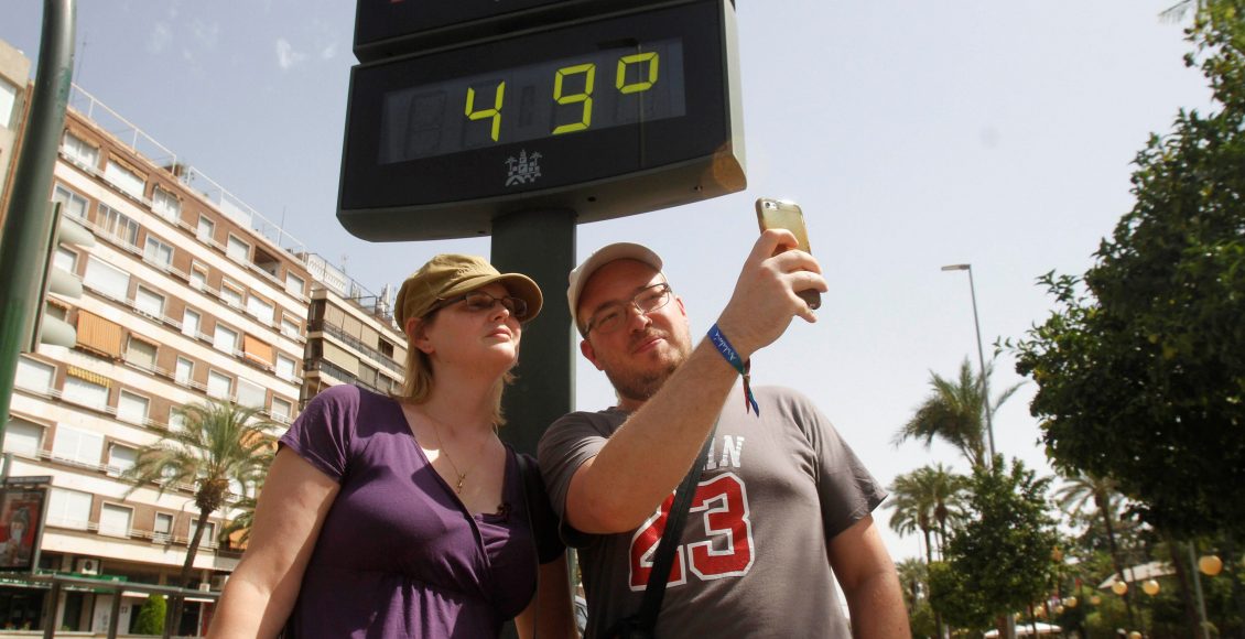 Turistas se hacen una foto junto a un termómetro de Córdoba que marca 49ºC debido a la ola de calor de los últimos días.