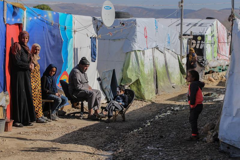 Refugiados sirios sentados al sol frente a sus tiendas de campaña, después de que estas se hundieran con el agua de lluvia en el Líbano.